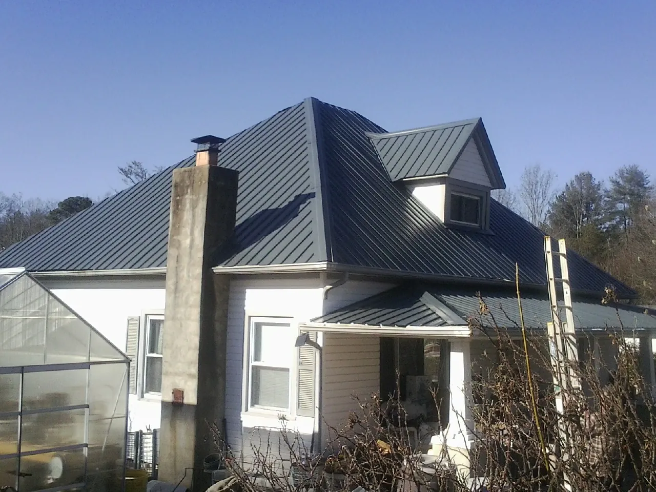 Dark blue standing seam metal roof on a white farmhouse with dormer — Slate & Tile Roof Repair by Roofing Brothers in Claridge