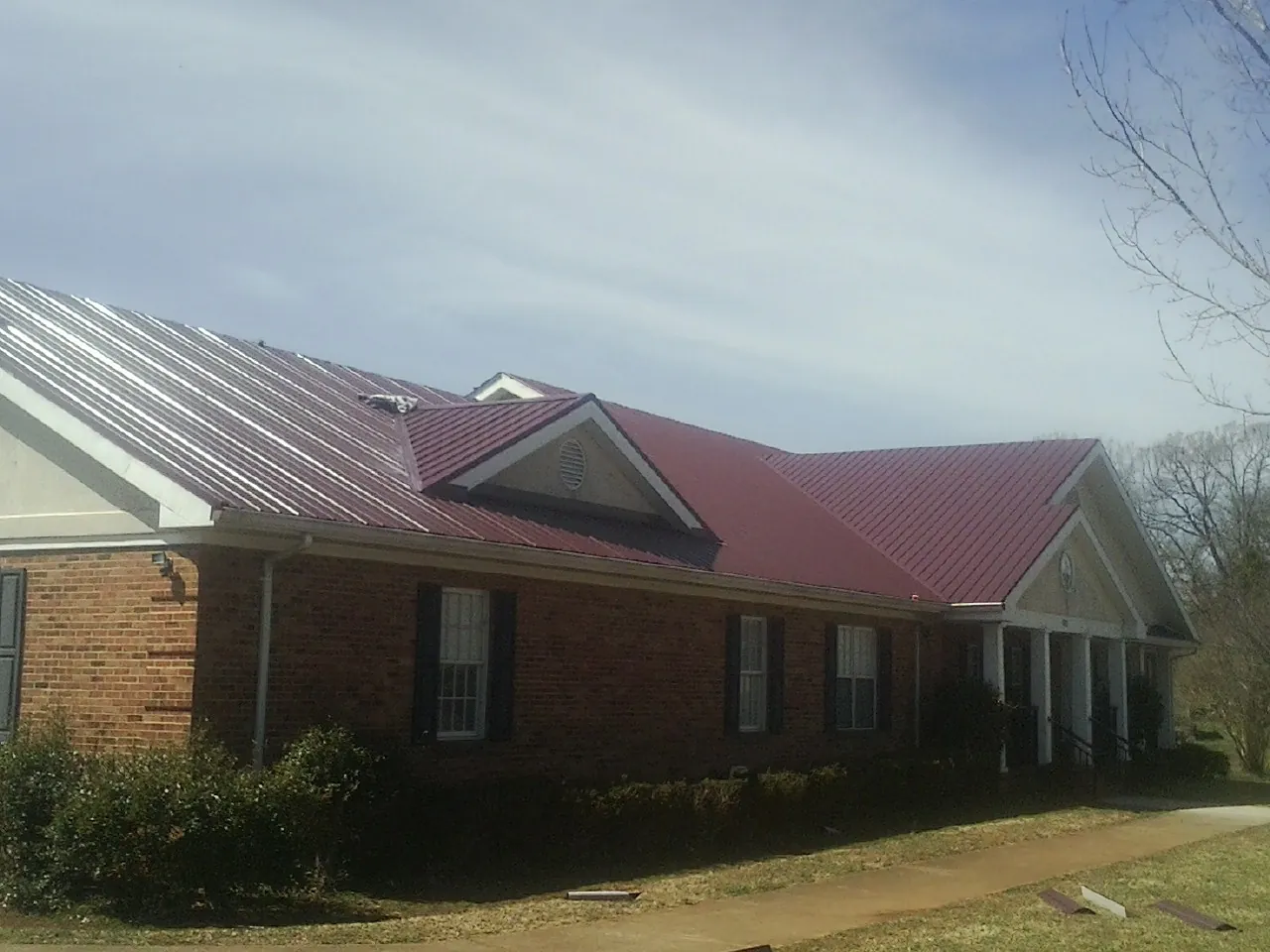Red metal roof with gabled entries on a long brick building, from a Hail Damage Roof Repair job in Claridge