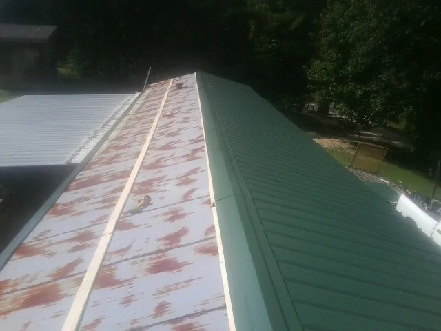 Old rusted panels beside newly installed green metal roofing — Wind Damage Roof Repair by Roofing Brothers in Claridge
