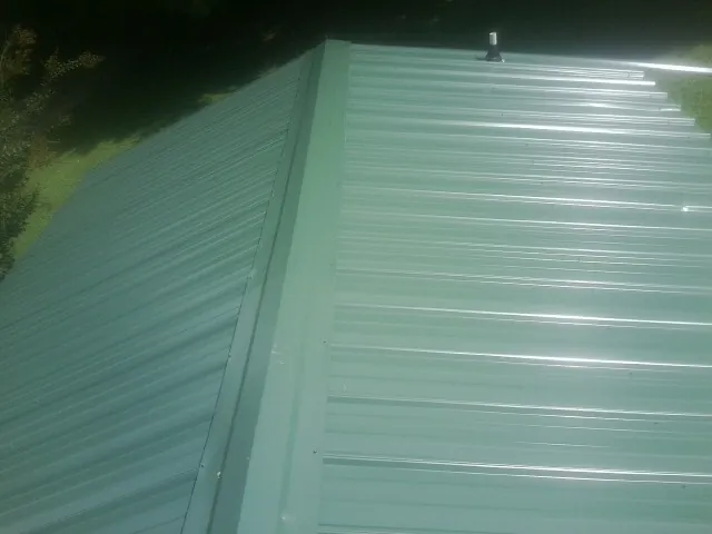New green metal panels meeting at the ridge of a roof — Flat Roof Repair work by our crew in Claridge
