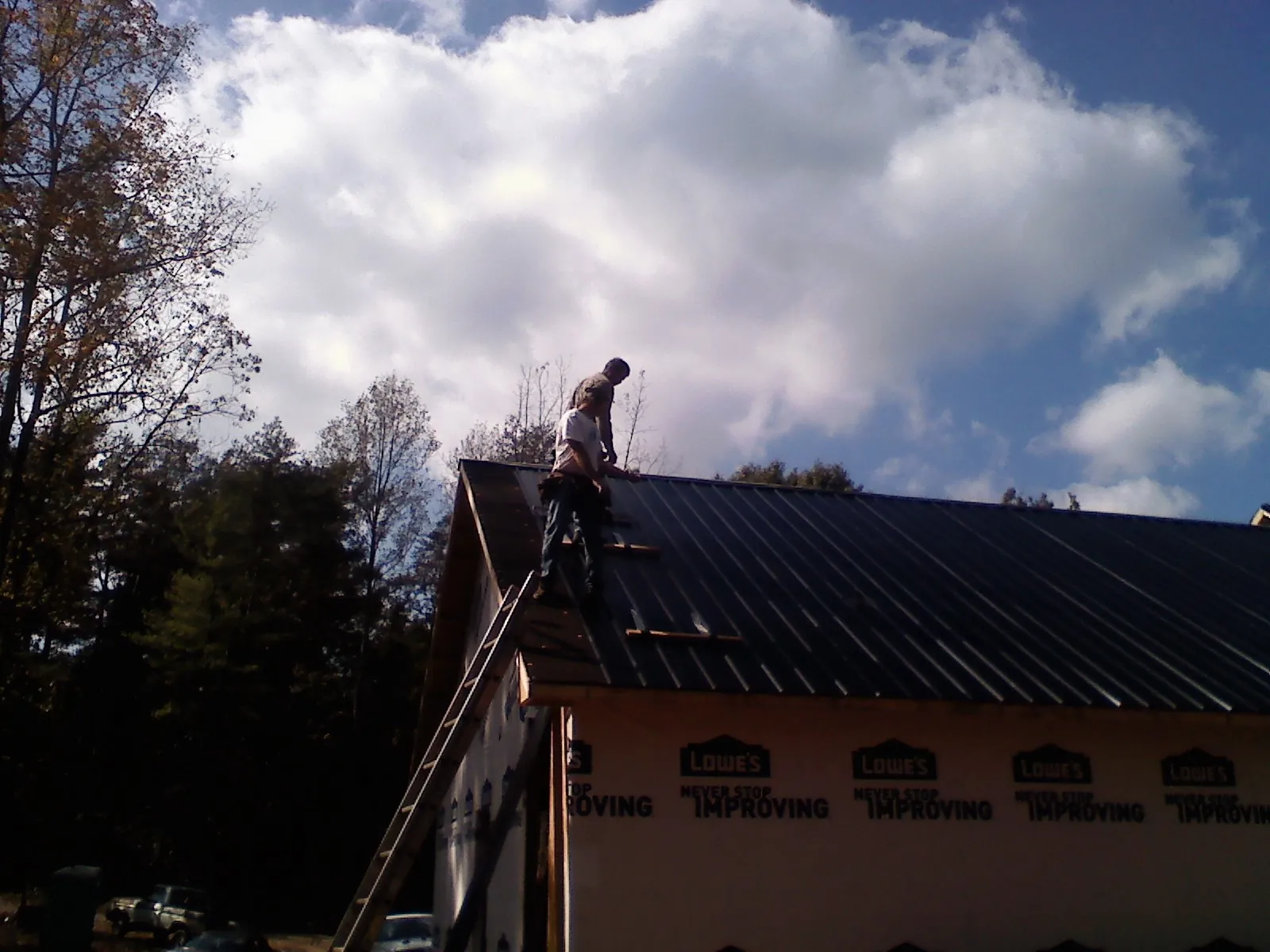 Roofer fastening dark metal panels high against a cloudy sky, from a Roof Inspection job in Claridge